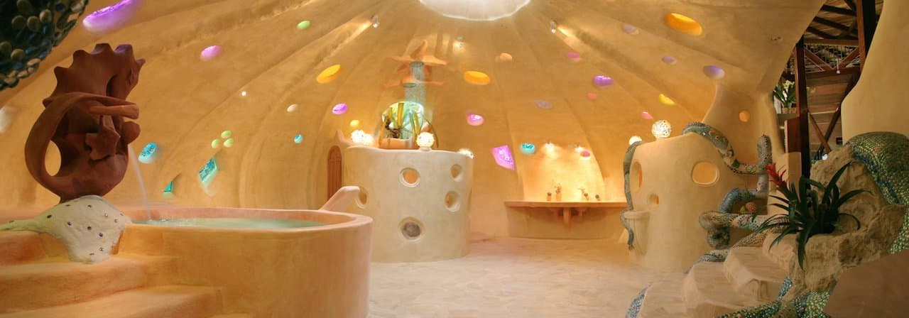 Panoramic view of the Gaudí-influenced mosaic bathroom — curved cream plaster walls inlaid with hundreds of coloured-glass discs