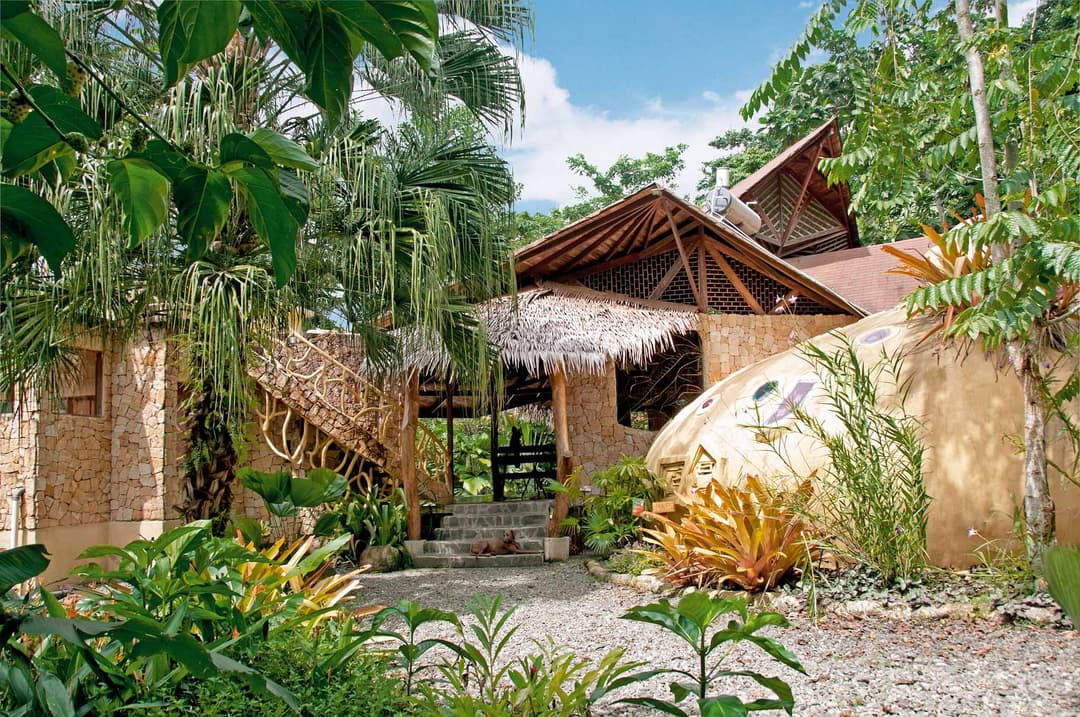 Front approach to the Beach Suite — thatched rancho beside the dome bathroom, palms and heliconia flanking the path