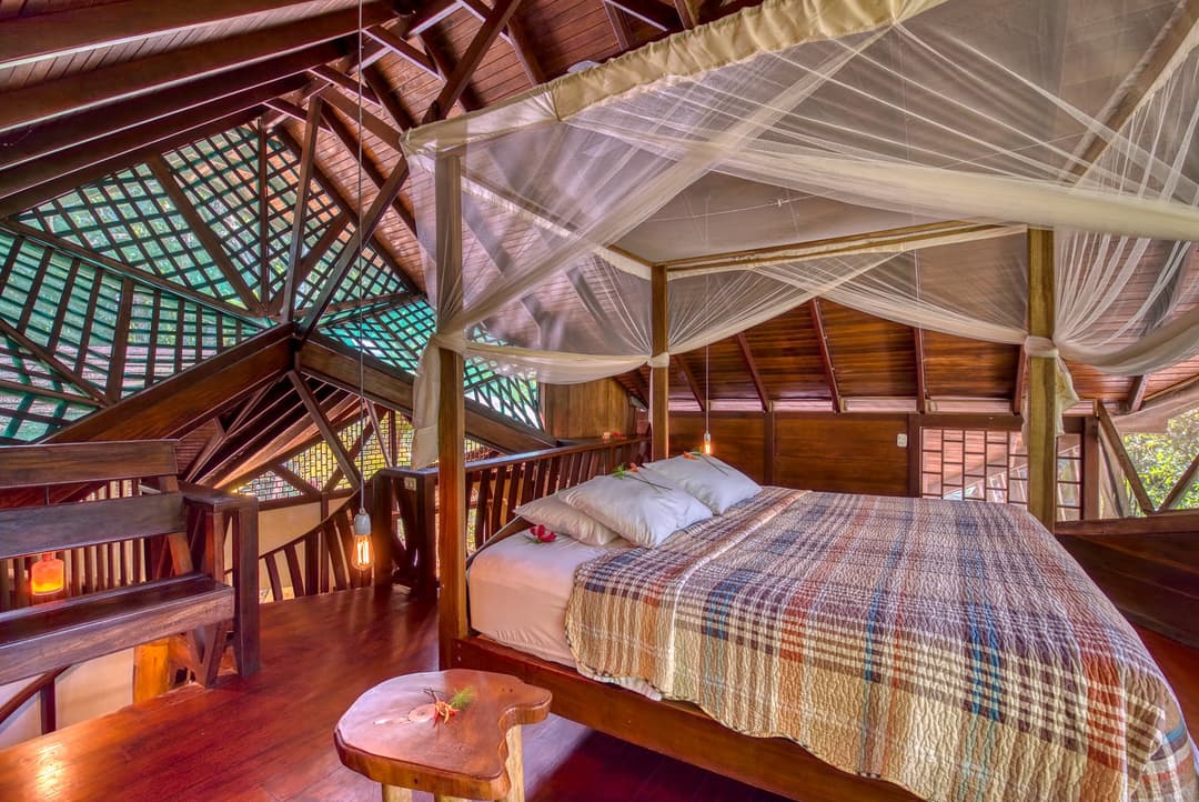 Upstairs master bedroom — king-size bed inside a four-post mosquito-net canopy, vaulted hardwood ceiling