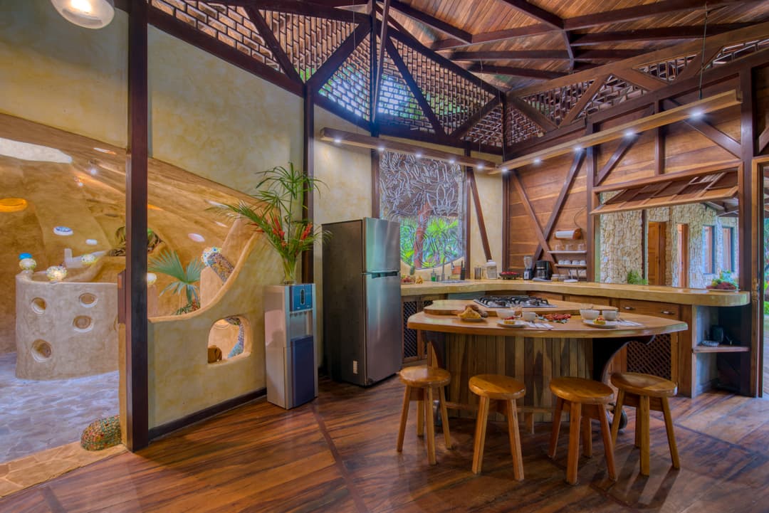Open main living area — hardwood floors, communal round dining table on carved stools, lattice-mesh A-frame ceiling