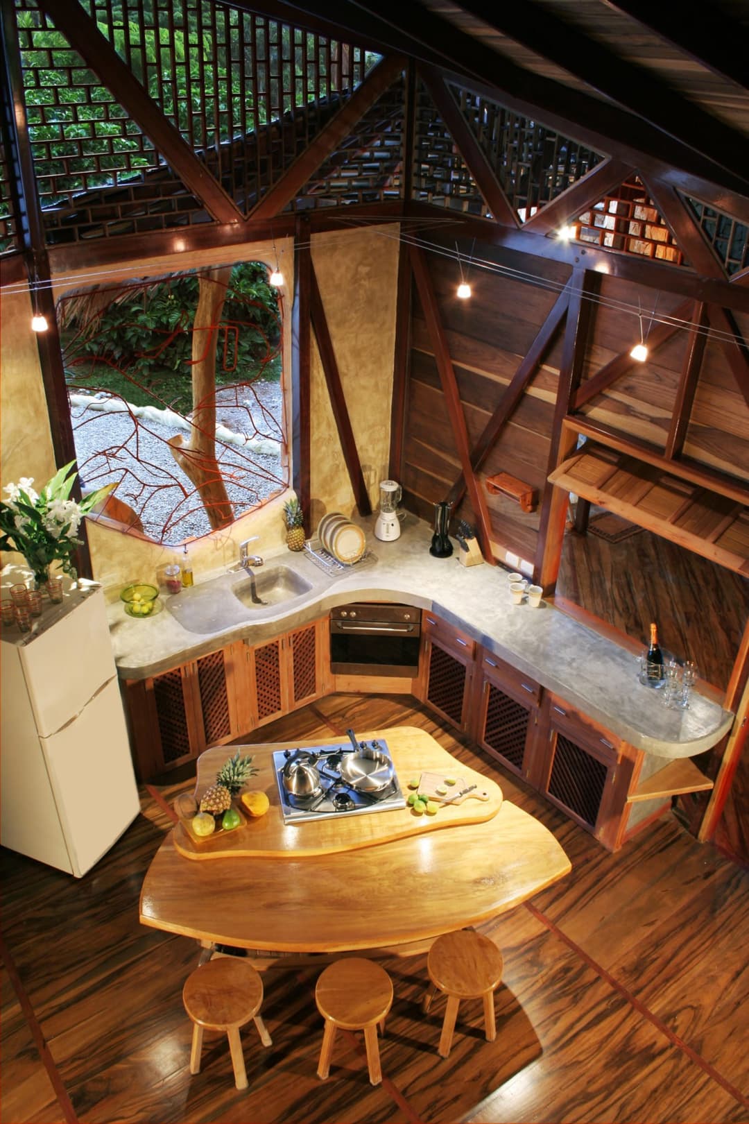 Top-down view of the kitchen — wood-trimmed counters, twin-burner stove, low fridge, beam-and-lattice ceiling